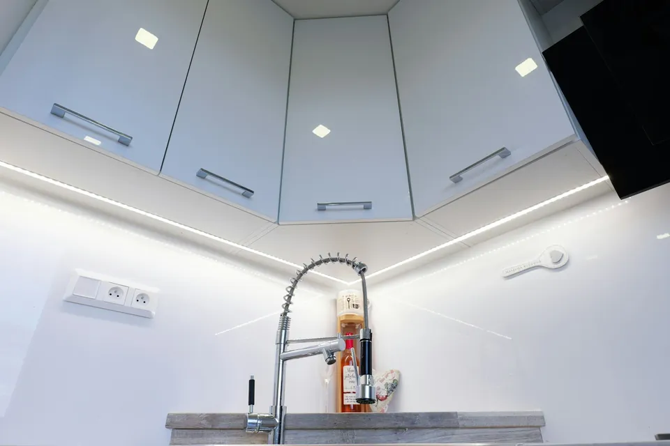 Glossy white kitchen corner with wall cabinets, under-cabinet strip lighting and a tall chrome spring-neck tap.