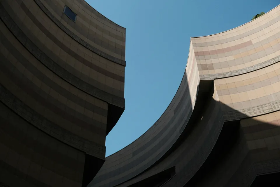 Low-angle view of curved, layered building facades framing a clear blue sky.