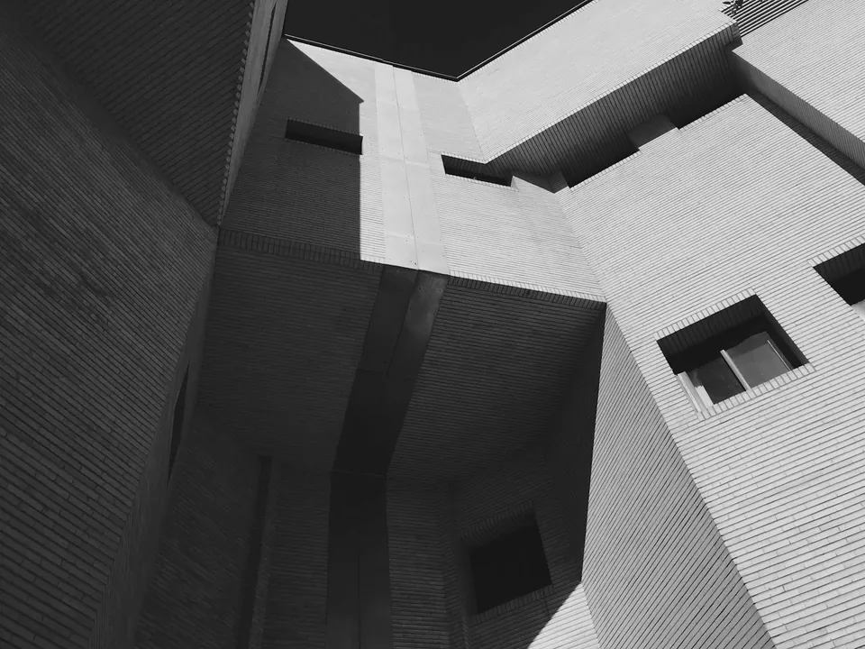 Black and white view looking up at angular brick walls that meet around a small patch of sky.