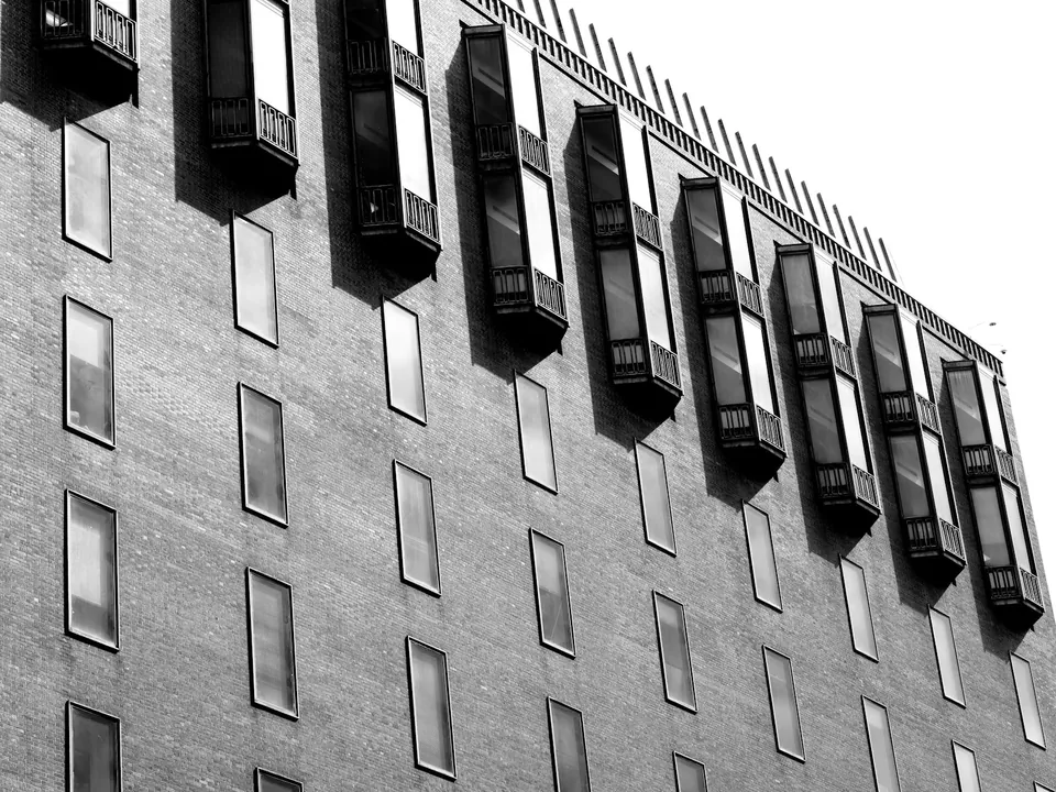 Black and white view of a tall brick building with a row of projecting box windows near the top.