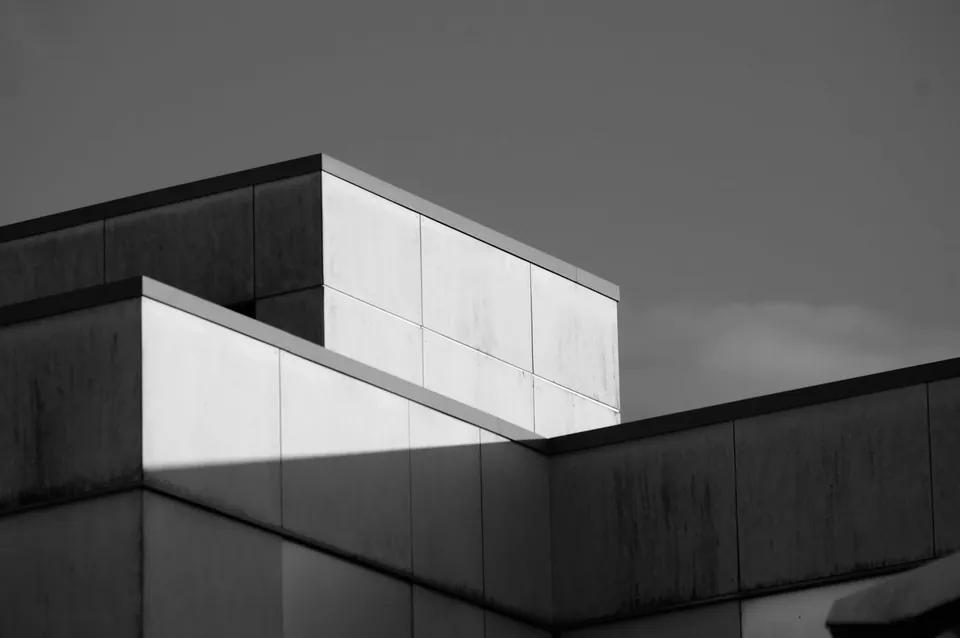 Black and white view of a flat-roofed building with stepped, panelled walls against a grey sky.