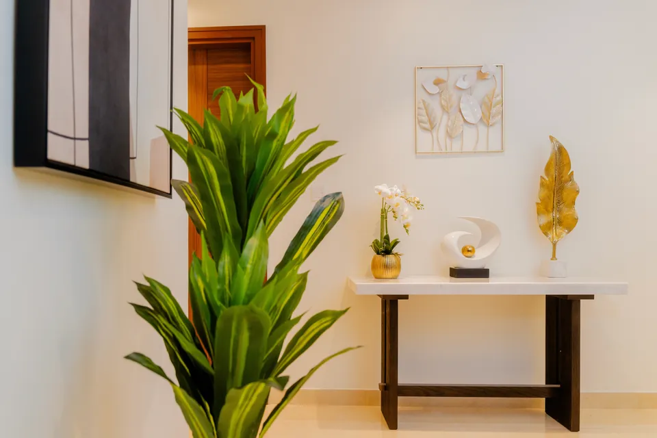 Imperial Avenue Apartment, Downtown Dubai: white console with gold leaf ornaments, a white orchid and a tall green plant.