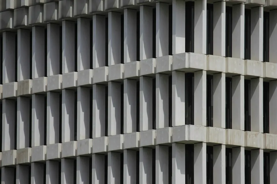Close-up of a grey building facade with a deep grid of vertical fins and horizontal ledges.
