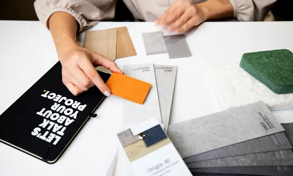 Hands sorting wood, grey and orange material samples beside a notebook reading Let's Talk About Your Project.