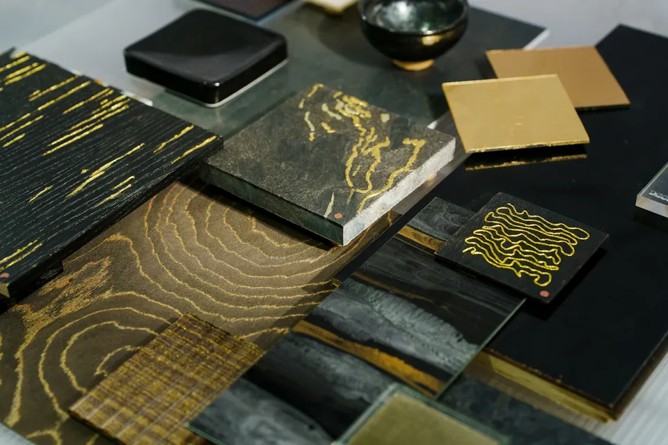 Close-up of dark material samples with gold veining and gold metallic tiles laid out on a table.