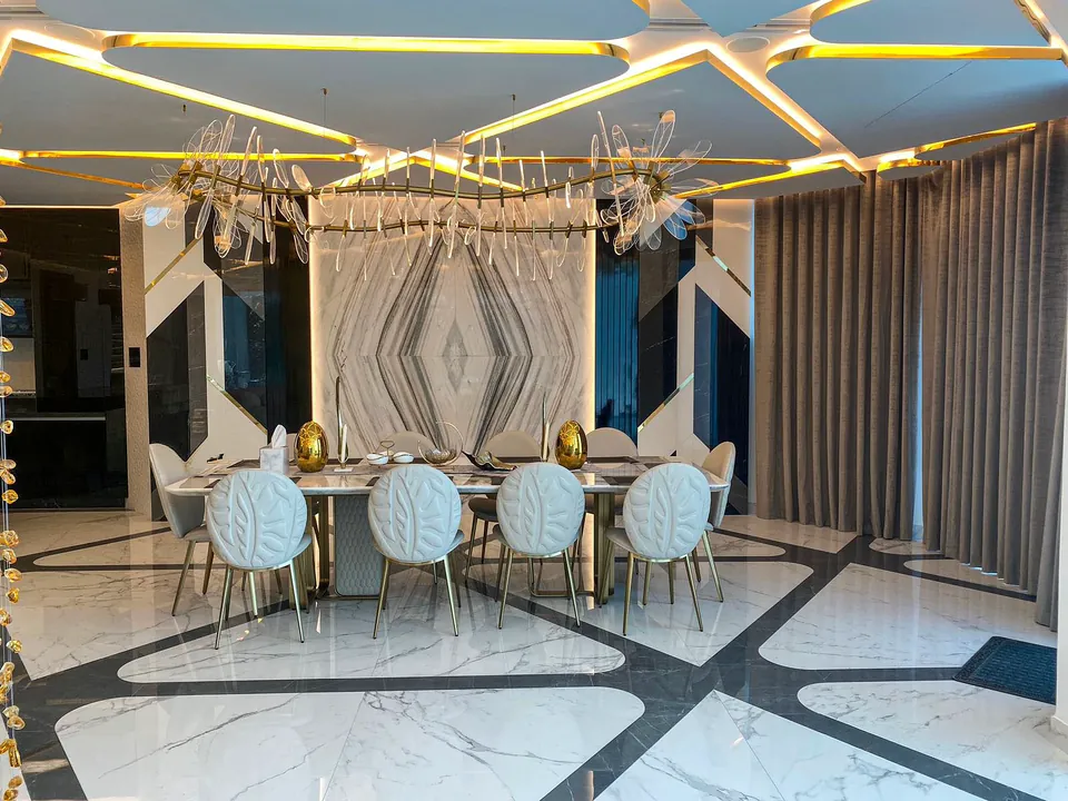 MK Villa, Palm Jumeirah: dining room with white shell-back chairs, a crystal chandelier and a marble-look feature wall.