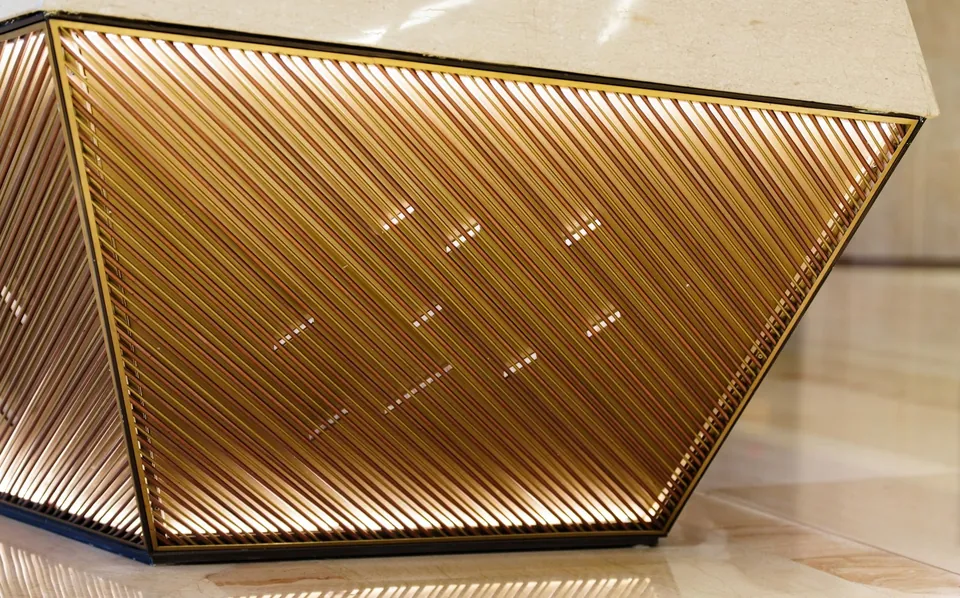 Faceted angular counter clad in diagonal gold slats with small lights, set on a pale polished floor.
