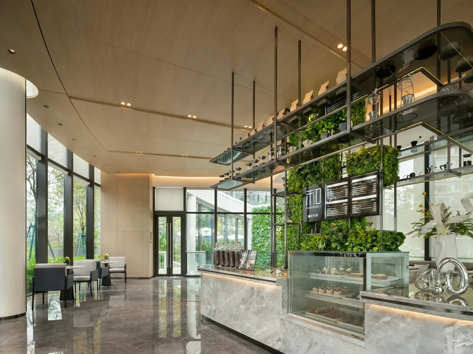 Café counter with glass display cases, a green plant wall and suspended glass shelving in a tall glazed space.
