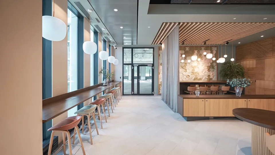 Long bright space with a wooden counter and stools along the windows, globe pendants and a slatted wood ceiling.