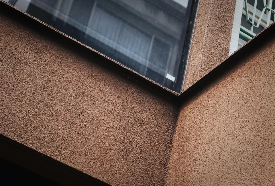 Close-up of textured terracotta-coloured walls meeting at an angle beneath a glass window.