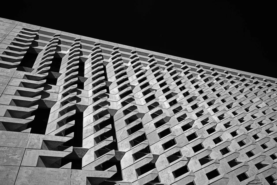 Black and white facade of angled geometric blocks forming a deep repeating pattern against a dark sky.