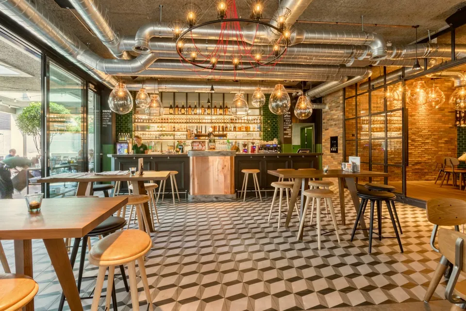 Café bar with a cube-pattern floor, wooden tables and stools, exposed ducts and glass globe pendants.